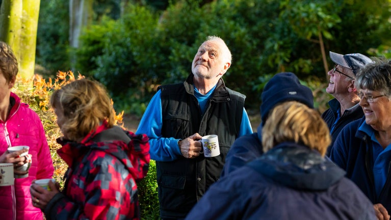 A volunteer looking up at the trees smiling while enjoying a coffee break